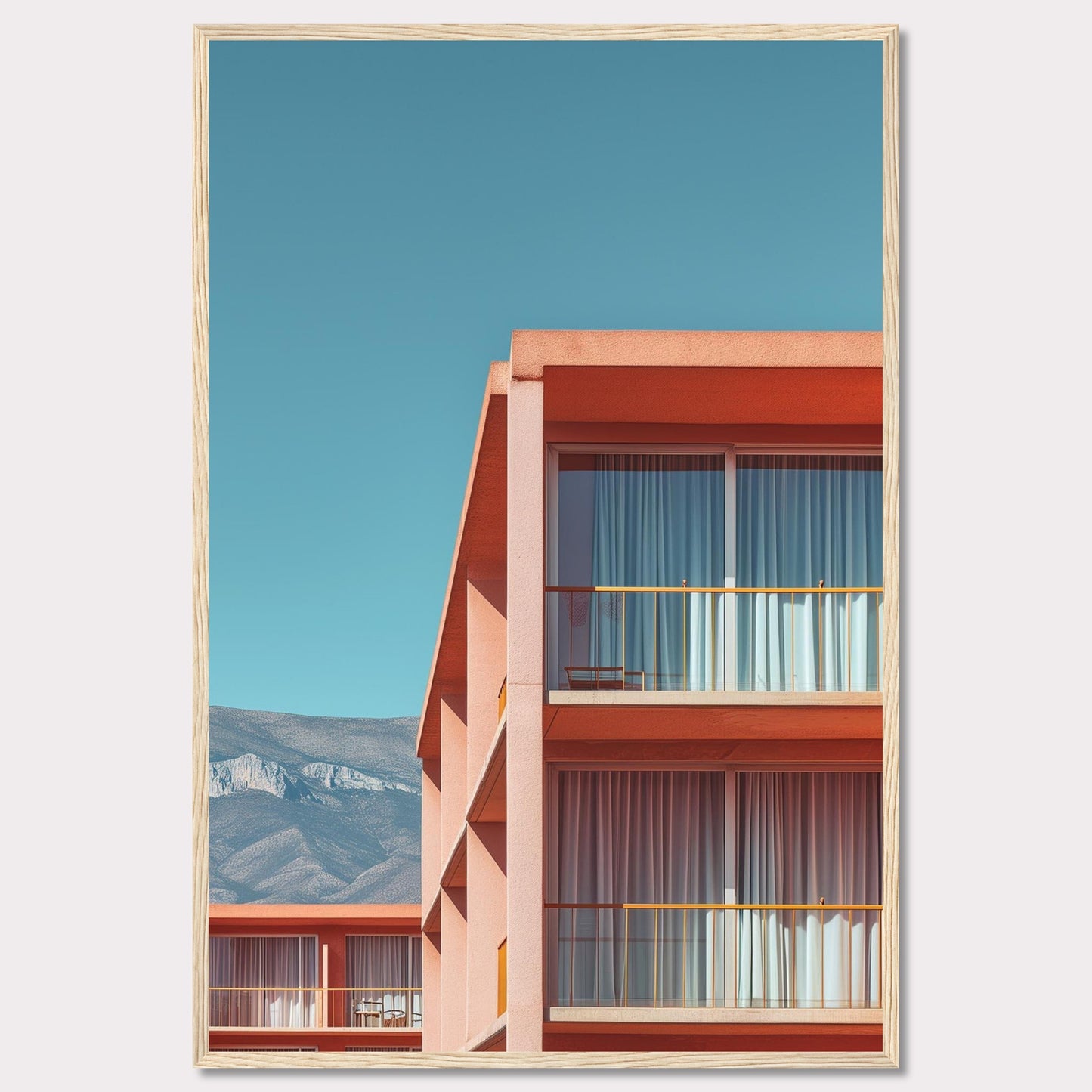 This captivating image showcases a modern building with a vibrant orange facade under a clear blue sky. The structure features large glass windows with white curtains, and balconies equipped with minimalistic furniture. In the background, majestic mountains add a serene touch to the scene.