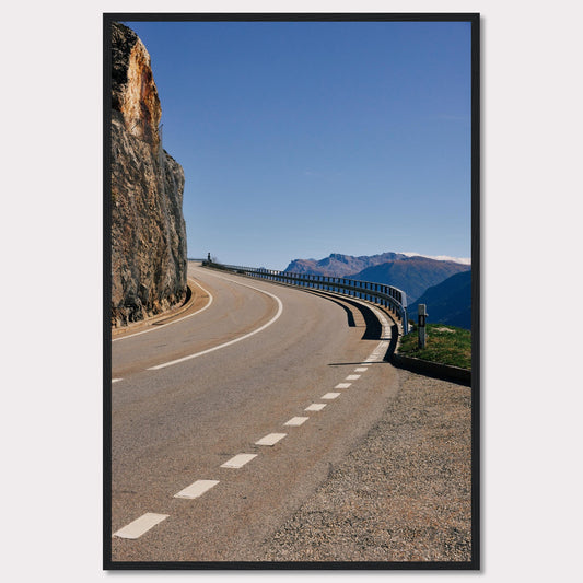 This captivating photograph showcases a winding mountain road bordered by a sheer rock face on one side and a protective guardrail on the other. The clear blue sky and distant mountain range add to the scene's serene beauty.