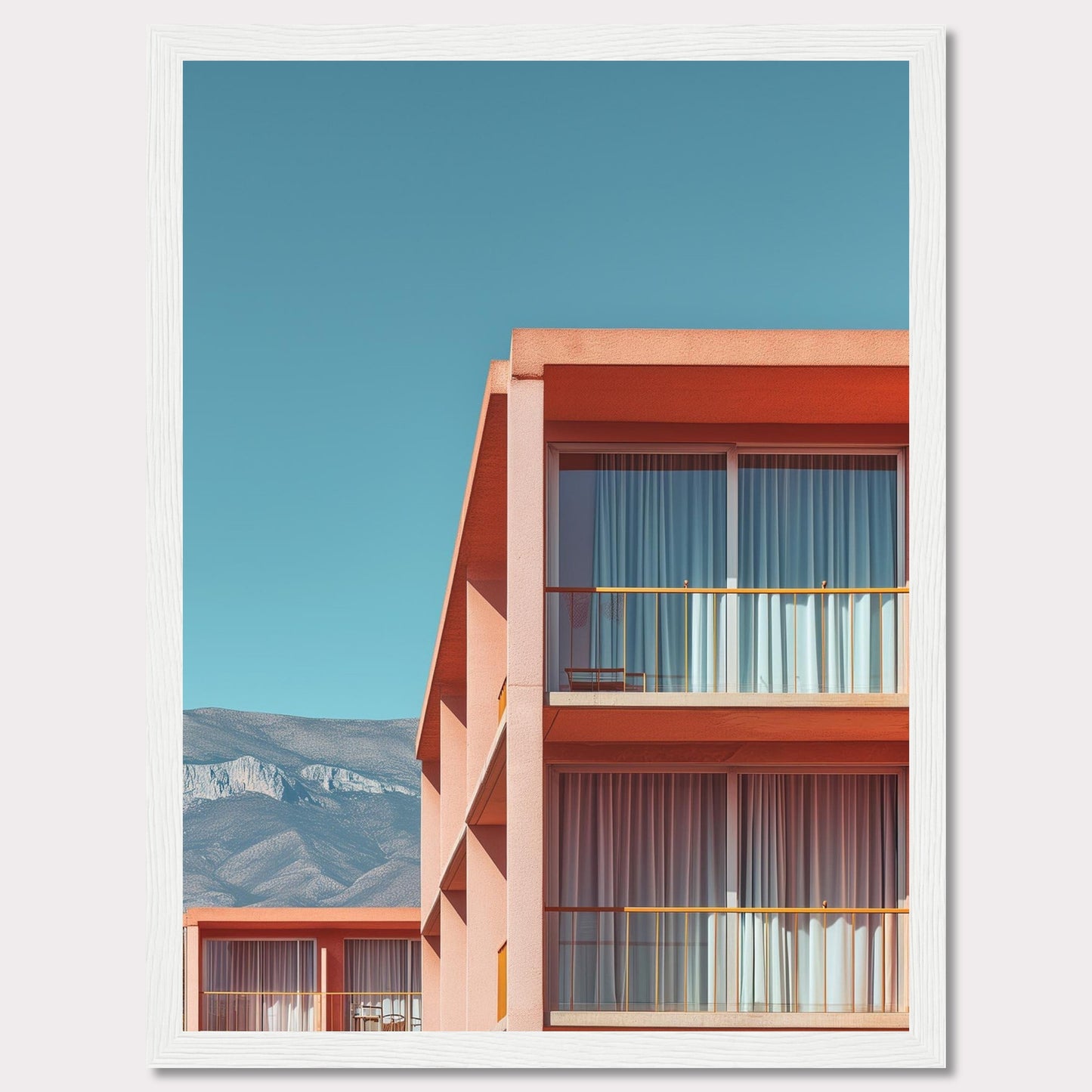 This captivating image showcases a modern building with a vibrant orange facade under a clear blue sky. The structure features large glass windows with white curtains, and balconies equipped with minimalistic furniture. In the background, majestic mountains add a serene touch to the scene.