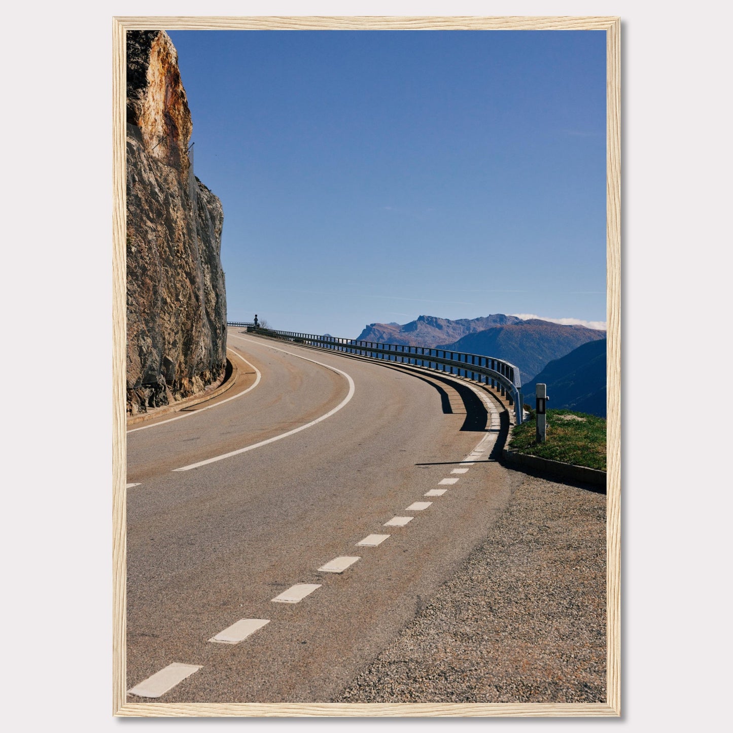 This captivating photograph showcases a winding mountain road bordered by a sheer rock face on one side and a protective guardrail on the other. The clear blue sky and distant mountain range add to the scene's serene beauty.