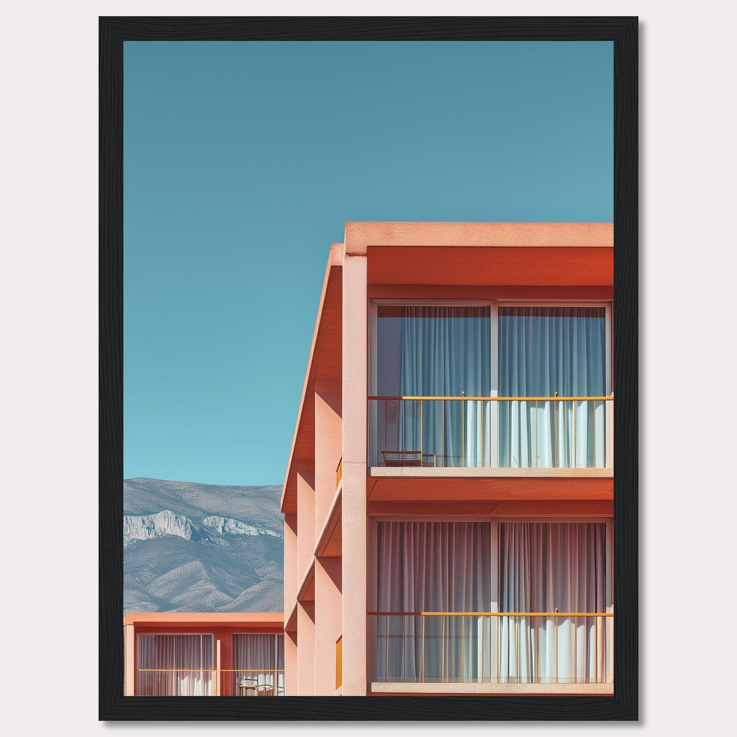 This captivating image showcases a modern building with a vibrant orange facade under a clear blue sky. The structure features large glass windows with white curtains, and balconies equipped with minimalistic furniture. In the background, majestic mountains add a serene touch to the scene.