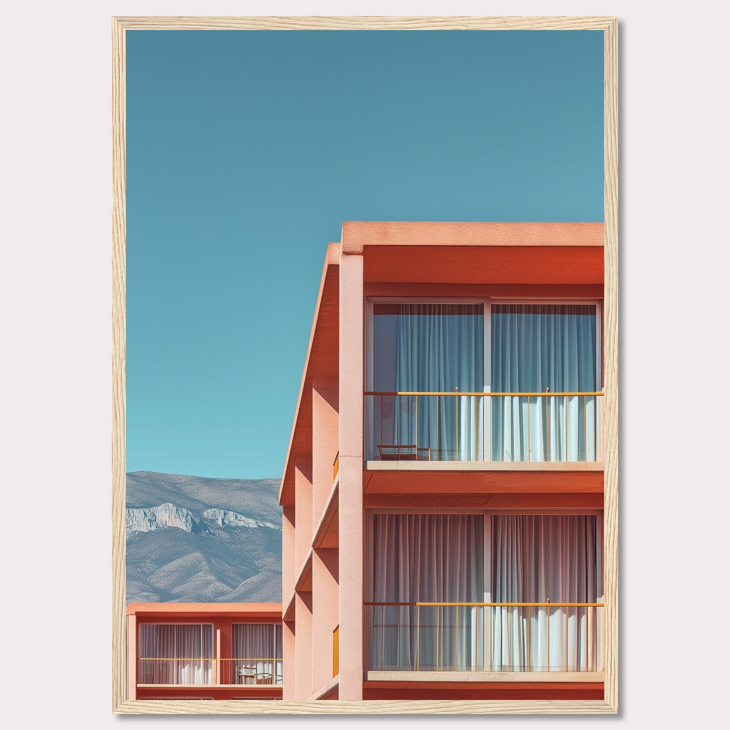 This captivating image showcases a modern building with a vibrant orange facade under a clear blue sky. The structure features large glass windows with white curtains, and balconies equipped with minimalistic furniture. In the background, majestic mountains add a serene touch to the scene.