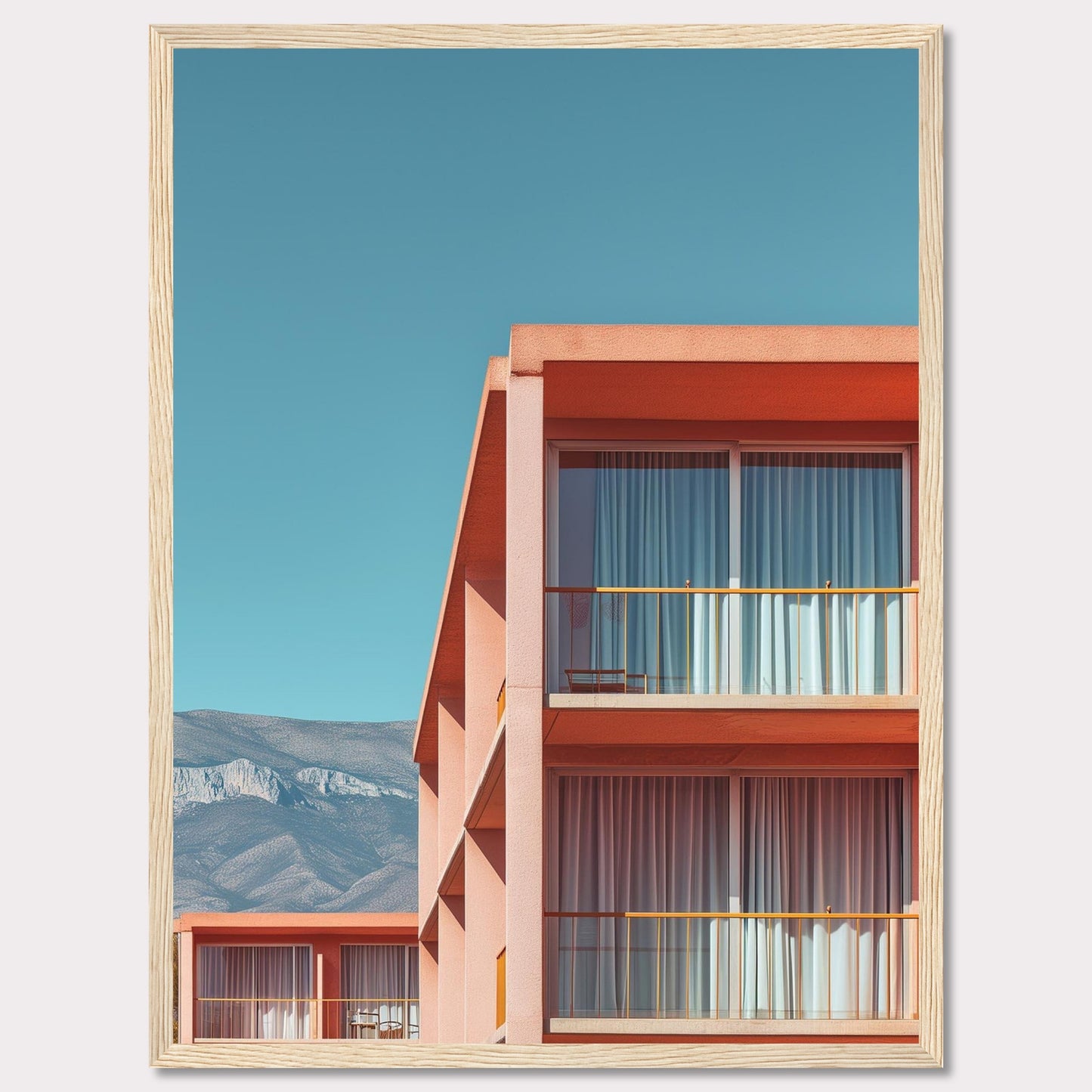 This captivating image showcases a modern building with a vibrant orange facade under a clear blue sky. The structure features large glass windows with white curtains, and balconies equipped with minimalistic furniture. In the background, majestic mountains add a serene touch to the scene.